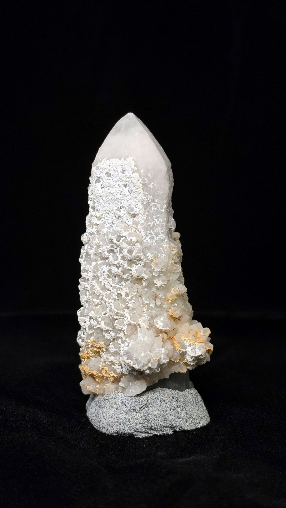 修長白色標本的另一角度,上段露出較寬的平整尖面,下段小晶面外突並散布黃褐色區域。