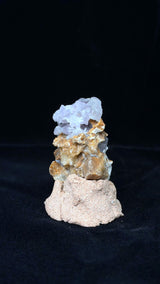 較窄視角下的直立標本，頂部淺紫晶體向左伸展，下方褐色塊面突出，置於粉米色底座上。