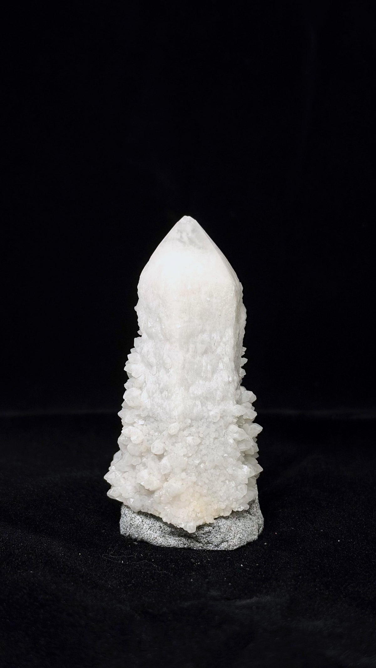 乳白色尖頂柱狀標本，下段密集細小晶體向兩側展開，置於灰色斑點底座上。